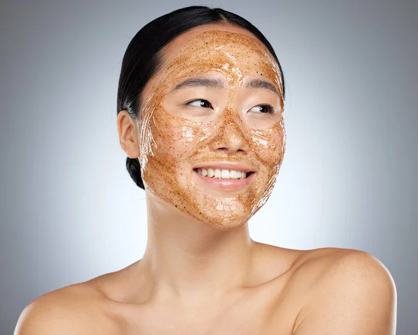 Exfoliate face mask for beauty skincare, natural product for healthy skin and clean cosmetic wellness for body against grey mockup studio background. Happy, smile and healthcare on Asian woman model.