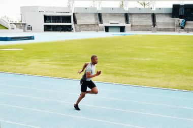 Vücudumu maratona hazırlıyorum. Yakışıklı genç bir sporcunun açık hava antrenmanı sırasında tek başına koşu sahasında uzun bir çekim.