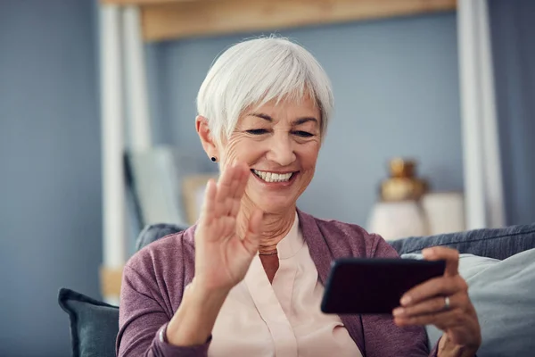 こんにちは 自宅のソファでビデオ通話中にこんにちは手を振っ幸せなシニア女性 — ストック写真