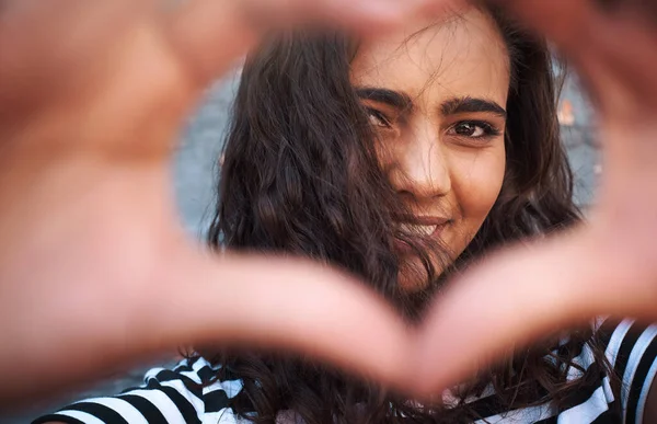 stock image Love surrounds us all. Portrait of a young woman making a heart shape with her hands against a grey wall