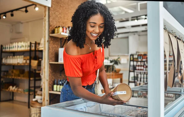 Shopping, supermarket and customer with product in groceries freezer for food choice, store sale or price check. Commerce, retail and grocery of black woman in eco friendly shop happy with decision.
