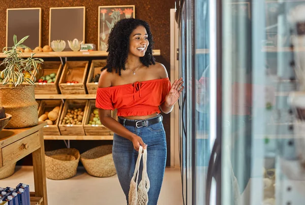 Black woman, grocery shopping and supermarket, customer and food, smile by refrigerator and happy with retail discount. Young, cold storage product and organic with fresh groceries, sale and buy