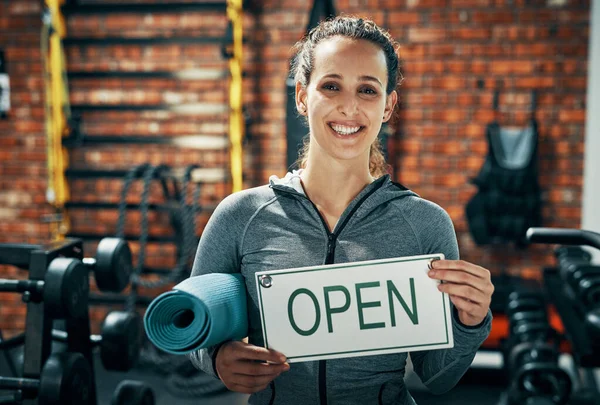 Were open and ready to get you in shape. a gym instructor holding up a open sign