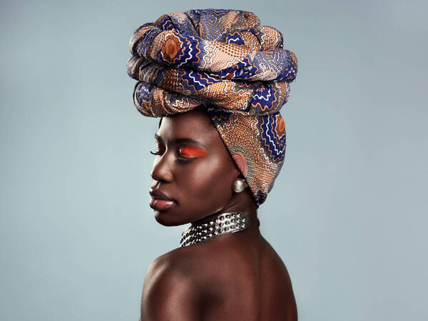 The head turning style of a head wrap. Studio shot of a beautiful young woman wearing a traditional African head wrap against a grey background