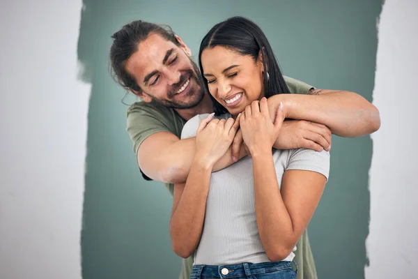 Happy, couple and hug for love, home improvement and smile against a painted wall background. Man and woman smiling for creative interior design in relationship, painting or house renovation together.