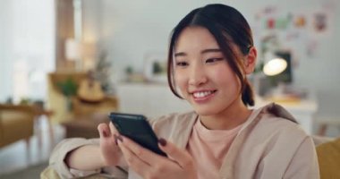 Asyalı kadın, telefon ve sosyal medya evdeki oturma odasındaki kanepede gevşeyen iletişim için gülümsüyor. Cep telefonunda mesajlaşmak, sohbet etmek ya da gezinmek için gülümseyen mutlu Çinli kadın..