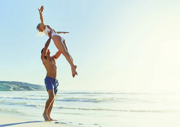 夏天只不过是无穷无尽的欢乐时光 一个年轻人把他的女朋友抬到海滩上的空中 — 图库照片