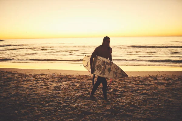在惊心动魄的一面抓住你 一个在海滩上背着冲浪板的年轻人 — 图库照片