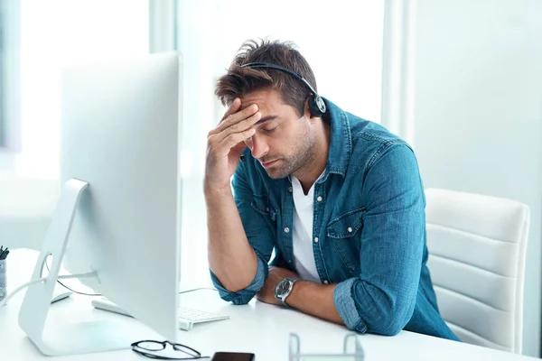Stock image I really need a miracle right about now. a young male call centre agent suffering from a headache in his office