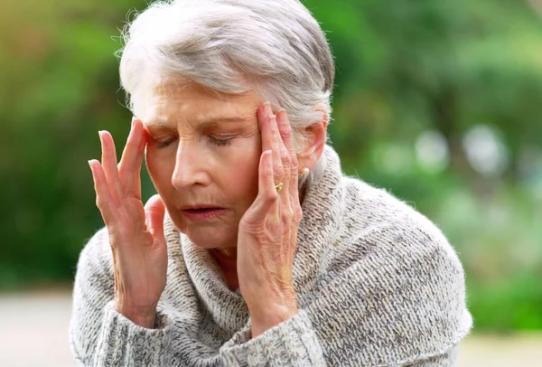 Dam you old age. a stressed out elderly woman seated on a bench and holding her head in discomfort outside in a park