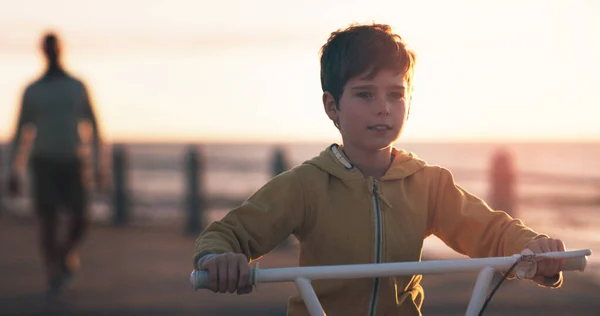 stock image Riding away into the sunset. an adorable little boy riding a bicycle at the beach with his father watching in the background