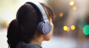 Müzik onu nereye götürürse oraya gider. Kentte yürürken kulaklıkla müzik dinleyen tanınmayan bir kadının yakın plan fotoğrafı.