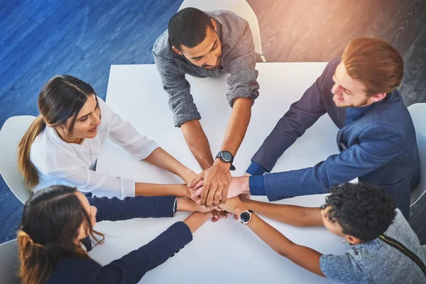 With all of us working together were bound to succeed. High angle shot of a group of young businesspeople joining their hands together in unity during a meeting at work