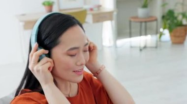 Müzik, kulaklıklar ve oturma odasındaki kanepede oturan kadın. Canlı yayın abonelik hizmeti ve motivasyon podcast çalışması için. Asyalı bir öğrenci bilgisayarında bir kanepede ses dinliyor ve daktilo yazıyor..