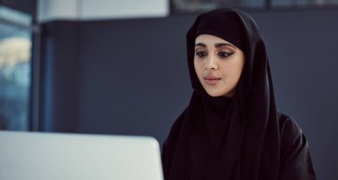 Sıkı çalış ve başarı seni takip edecek. Ofiste dizüstü bilgisayarıyla çalışan çekici, genç bir Arap iş kadını.