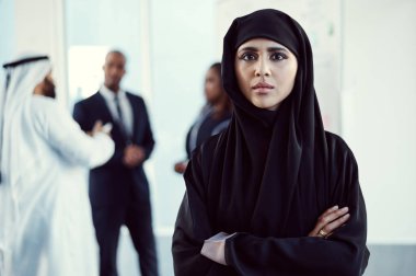 Yaptığım işe güvenim tam. Arkaplanda iş arkadaşlarıyla kollarını kavuşturmuş çekici, Arap bir iş kadınının portresi.
