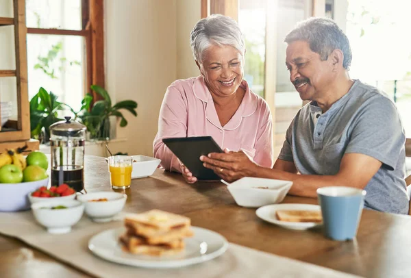 Take a look at this dear. a cheerful elderly couple browsing on a digital tablet together while having breakfast around a table at home