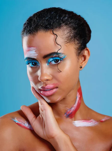 stock image The face of beauty is colourful. Studio portrait of a beautiful young woman covered in face paint posing against a blue background