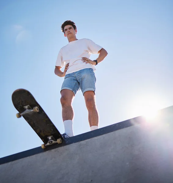 Blue sky, skateboard and young man from below on skate ramp ready for trick. Fitness, street fashion and urban sports, a skater in skatepark and summer sun for adventure, freedom and extreme sport