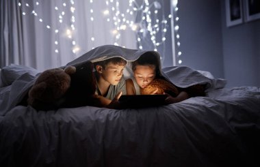 Bu kardeşler çizgi filmlerine bayılıyorlar. İki sevimli kardeş gece yatakta dijital tablet kullanıyorlar.