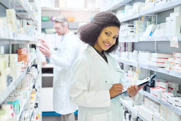 stock image Let me help you find the perfect remedy. a young woman doing inventory in a pharmacy with her colleague in the background