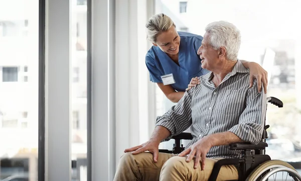 stock image How are you feeling today. a mature female nurse and her senior male wheelchair-bound patient in the hospital