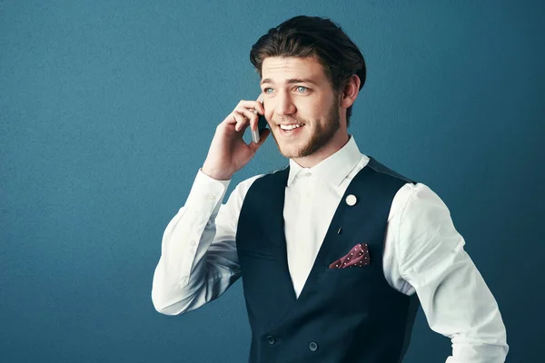 Ive been meaning to call you...Studio shot of a handsome young businessman making a phonecall against a blue background