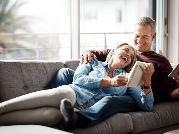 Share the love, share the laughter. a mature couple reading a book together while relaxing on the sofa at home