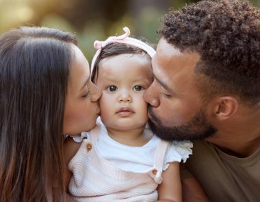 Anne, baba ve bebek bir bahçede sevgi, ilgi ve şefkatle kaynaşırken öpüşürler. Sevgi dolu, şefkatli ebeveynler küçük kızı öperken, doğal olarak dinlenmek için bağ kurarlar..