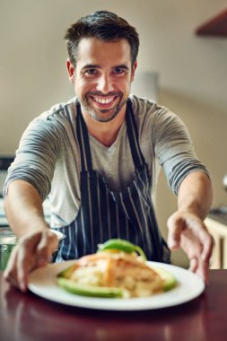 Aşçılık yenebilir bir aşktır. Evdeki mutfakta yemek servisi yapan genç bir adam.