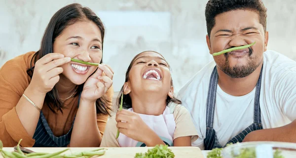 Happy asian family, play vegetables kitchen in portrait and smile together at table for bonding time. Mom dad, child happiness in comic home and health food in nutrition diet, dinner and kid cooking.
