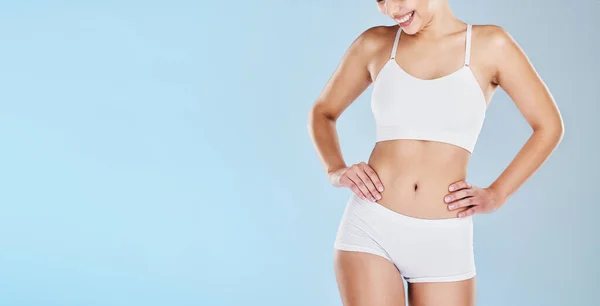 Closeup of fit woman showing her stomach and body in underwear or  sportswear, isolated against blue studio background with copyspace. Toned,  sporty model standing alone. Slim physique and flat tummy Stock Photo