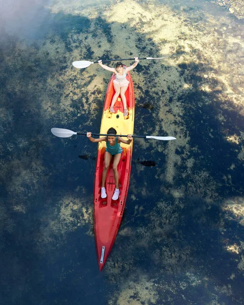 Friends kayak adventure, success and sport teamwork travel together outdoors. Happy women celebrate, cheering and winner paddle on vacation, river holiday or summer happiness break aerial view.