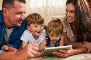 Teknolojiyi aile zamanına eklemek. Sevimli bir erkek ve kız kardeş dijital tablet kullanıyorlar ve aileleri evlerinde yerde.