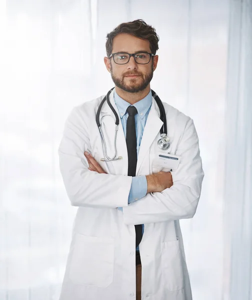 私はできるだけ早くあなたを直します 自信に満ちた若い男性医師が病院の中で腕を組んで立っている姿を切り取った肖像画 — ストック写真