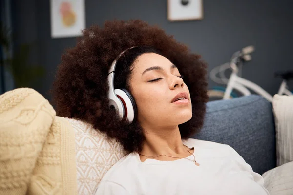 Music, relax and black woman on a sofa listening to radio, streaming or wellness podcast in a living room. Headphones, woman and rest on a couch with online audio track, meditation and playlist.