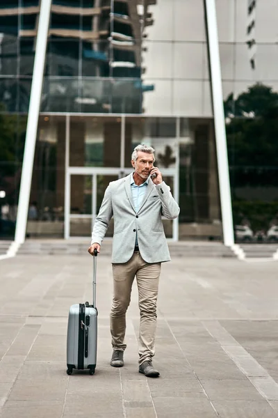 Never stop moving with your ambitions. a mature businessman talking on a cellphone while walking with a suitcase in the city