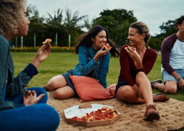 Dostlar, park ve bir parça mutluluk. Bir grup genç arkadaş parkta piknik yaparken birlikte pizza yiyorlar.
