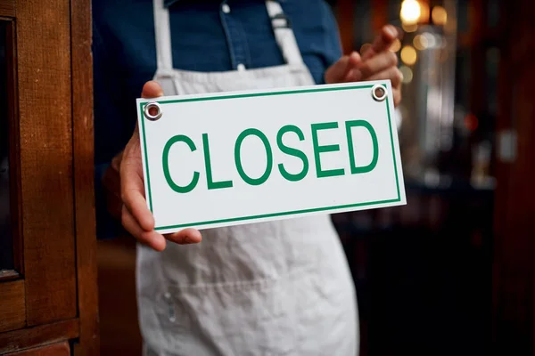 Another day of hard work done. Closeup of a unrecognizable business owner holding up a sign saying closed while standing under a doorway at a beer brewery during the day