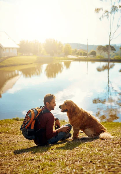 他绝对是这个男人最好的朋友 一个英俊的年轻人和他的狗坐在公园湖边的全景照片 — 图库照片