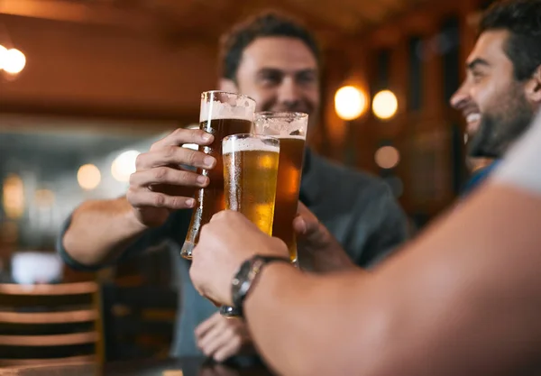 stock image Cheers to a good day of working. three cheerful young men having a celebratory toast with beer while sitting at a table inside of a beer brewery during the day