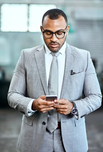 The man who makes things happen. a young businessman using a cellphone in an office