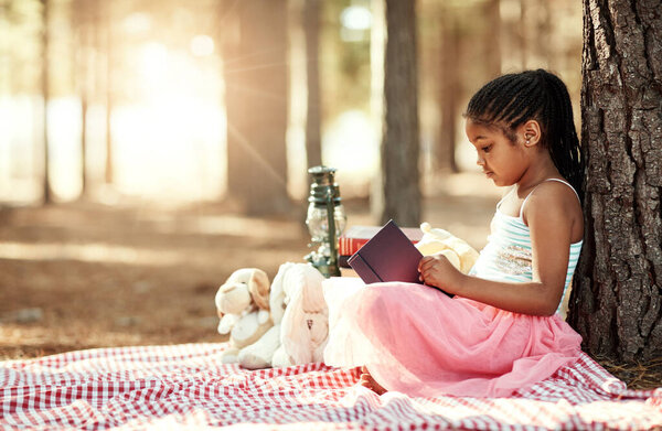 Books have a way of brightening a kids imagination. a little girl reading a book with her toys in the woods