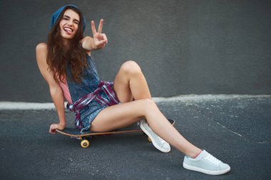 Kaykay yapmak için sörf tahtasına gidiyor. Gün boyunca dışarıda barış işareti gösterirken kaykayın üzerinde oturan neşeli genç bir kadının portresi.