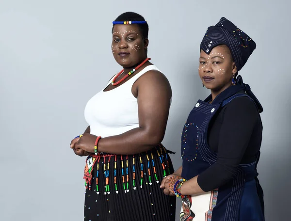 stock image Keeping it traditional. Studio shot of two confident middle aged woman looking into the camera while standing against a grey background