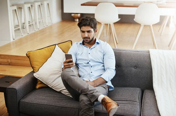 stock image Sending and receiving texts. a handsome young man sending a text while sitting on his sofa in the living room at home