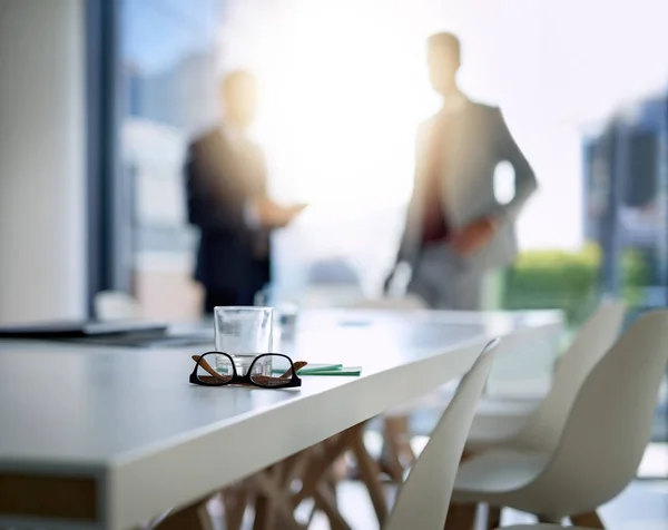 stock image Where business excellence happens. glasses and a glass on a boardroom desk with two businessmen blurred in the background