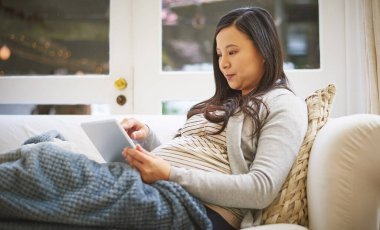 Hamilelik ipuçlarını ve tavsiyeleri inceliyorum. Evde dijital tablet kullanan hamile bir kadın.