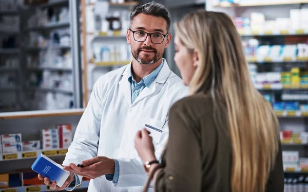 This should get you feeling better. a mature pharmacist assisting a young woman in a chemist