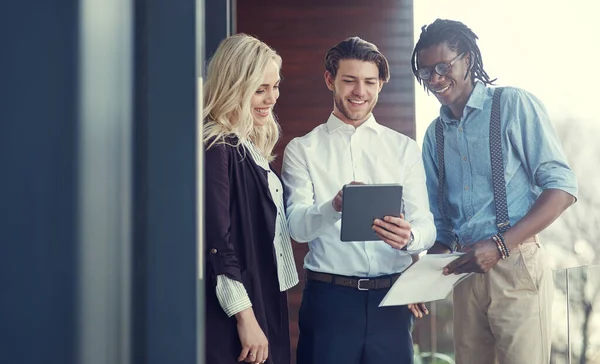 Stock image Explaining his idea. three young businesspeople using a tablet while standing outside on the office balcony